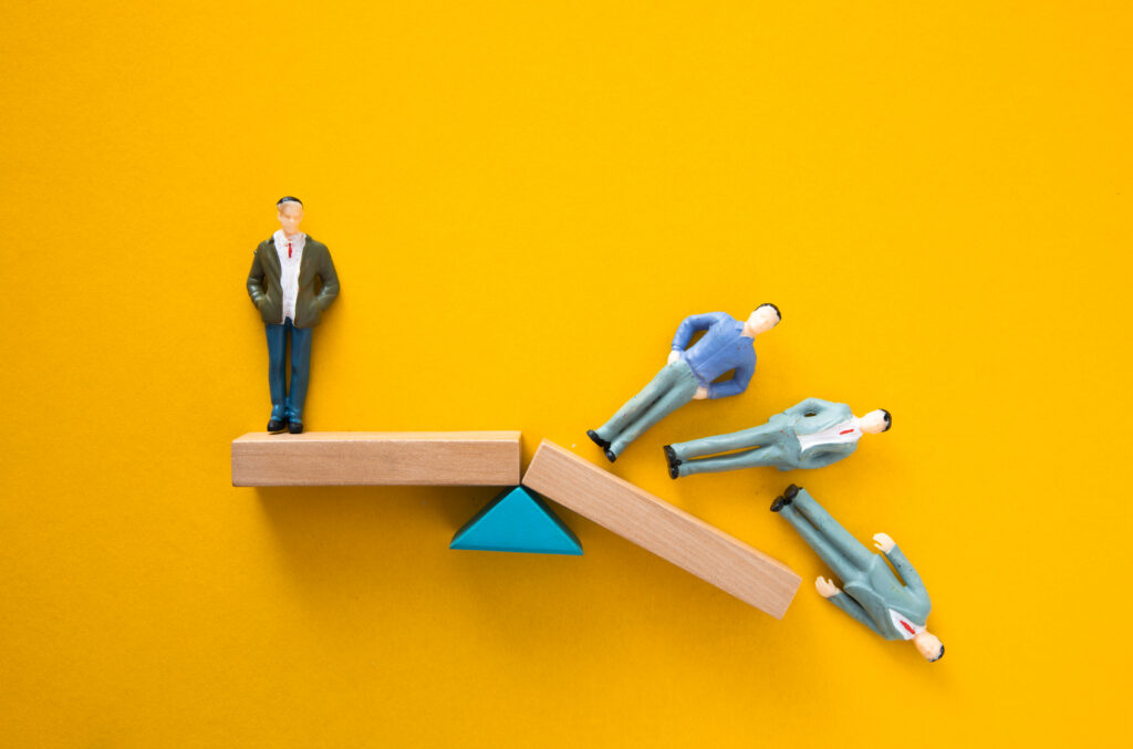 Miniature business figures balancing on a wooden platform symbolizing career stability.